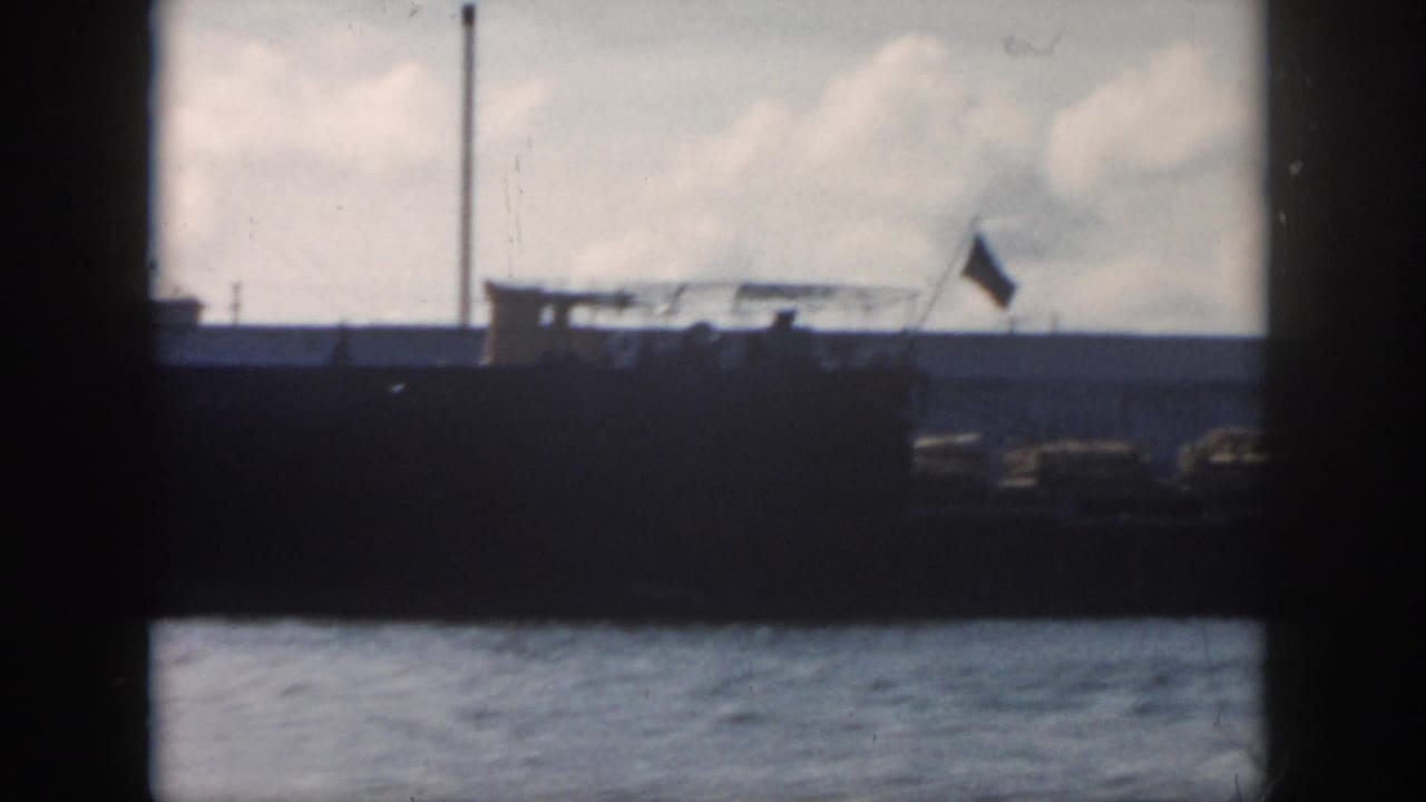 1958 New Orleans-area 8mm frame with a large vessel, raised flag, water foreground, and cloudy sky.