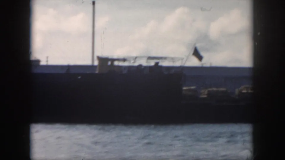 1958 New Orleans-area 8mm frame with a large vessel, raised flag, water foreground, and cloudy sky.