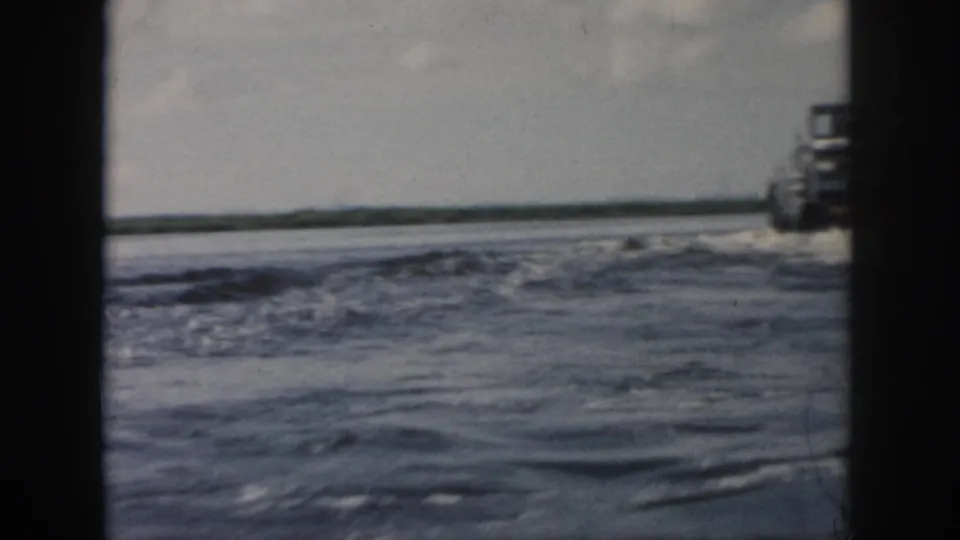 1958 New Orleans-area 8mm frame with rough water, low shoreline, cloudy sky, and a partial boat at frame edge.