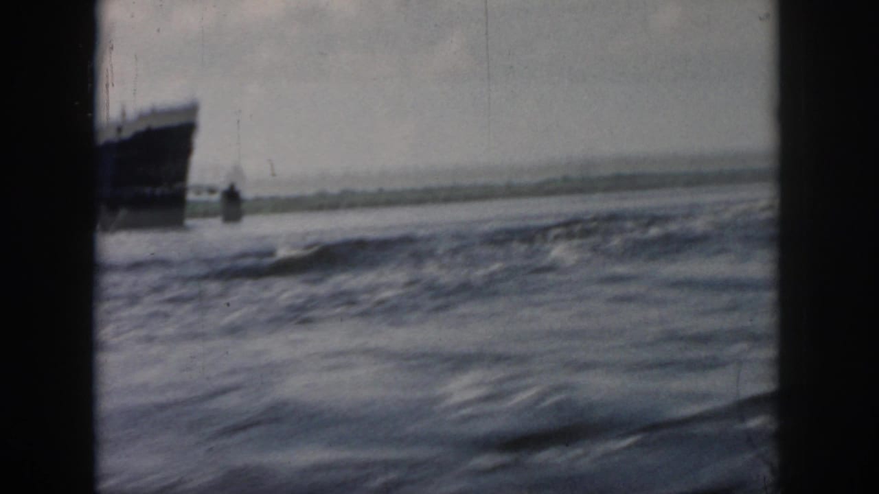 1958 New Orleans home-movie frame with a large ship partly visible at the left edge across moving water.