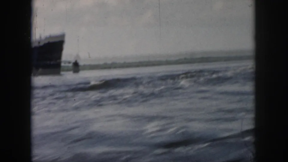 1958 New Orleans home-movie frame with a large ship partly visible at the left edge across moving water.