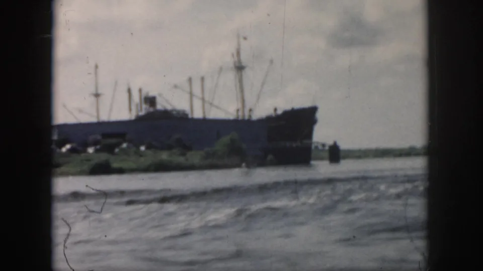 1958 New Orleans footage showing a large cargo ship near a low green shoreline across choppy water.