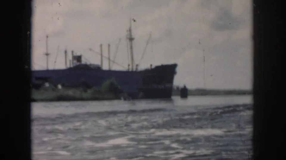 1958 New Orleans frame with a large ship near a low shoreline and textured water in the foreground.