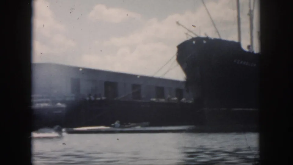 Soft 8mm view of a cargo ship bow and masts beside an industrial dock in 1958 New Orleans harbor footage.