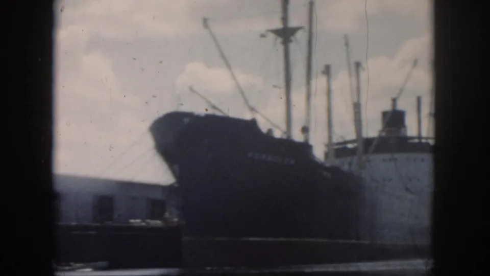 1958 New Orleans harbor frame showing the dark bow, masts, and pale superstructure of a cargo ship near the waterfront.
