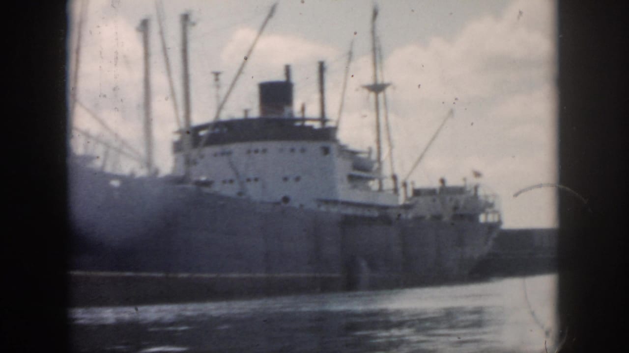 1958 New Orleans waterfront frame showing the cargo ship's side, white deckhouse, rigging, and moving water in front.