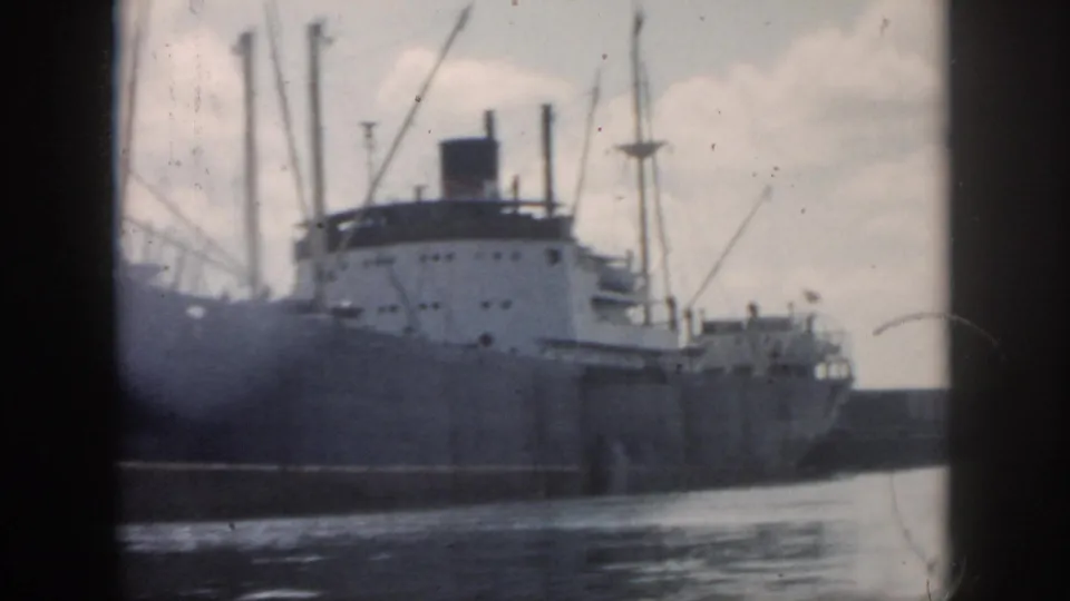 1958 New Orleans waterfront frame showing the cargo ship's side, white deckhouse, rigging, and moving water in front.