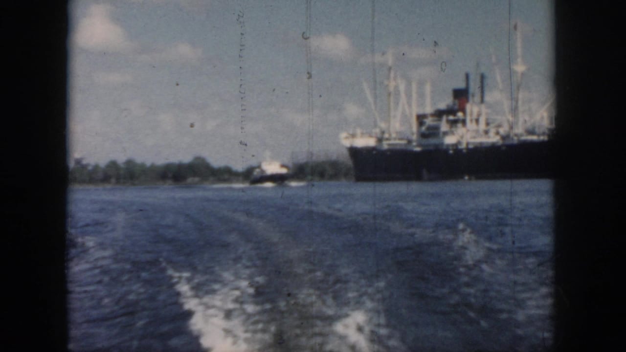 1958 New Orleans home-movie frame from a moving boat, showing wake, open water, a large ship, and a smaller vessel in the distance.