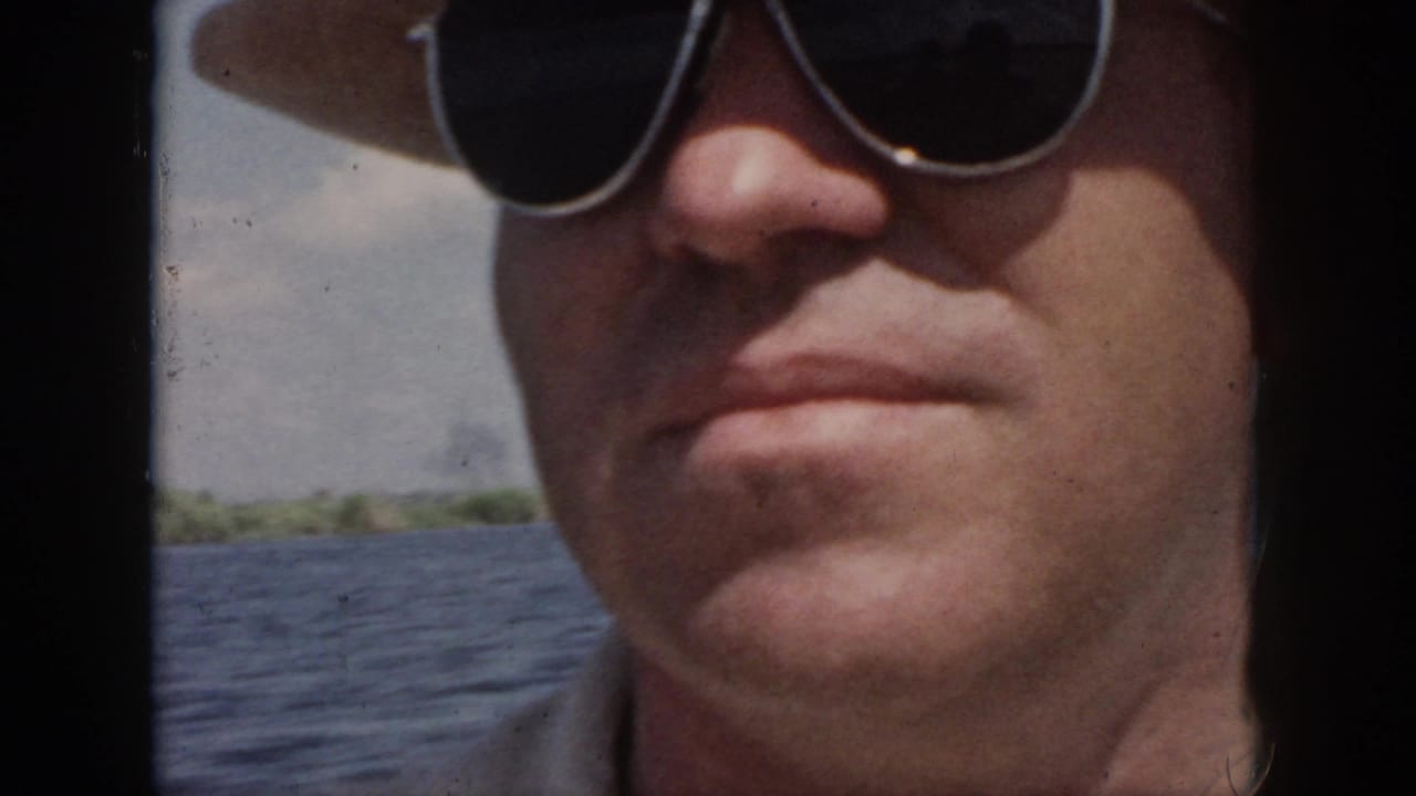 Close adult man wearing a hat and dark sunglasses on a boat near open water.