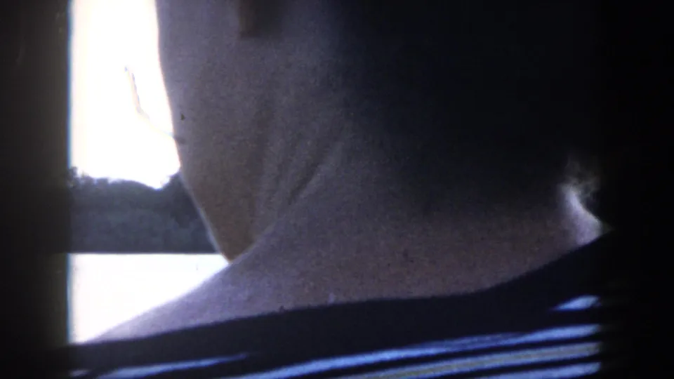 Close 8mm view from behind a boat passenger in a striped shirt, with bright water and shoreline shapes nearby.