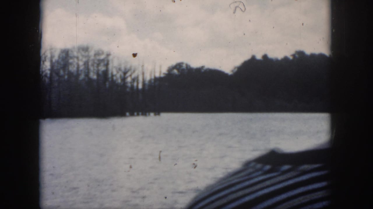 Lake seen through dark window framing with shoreline trees under a cloudy sky.