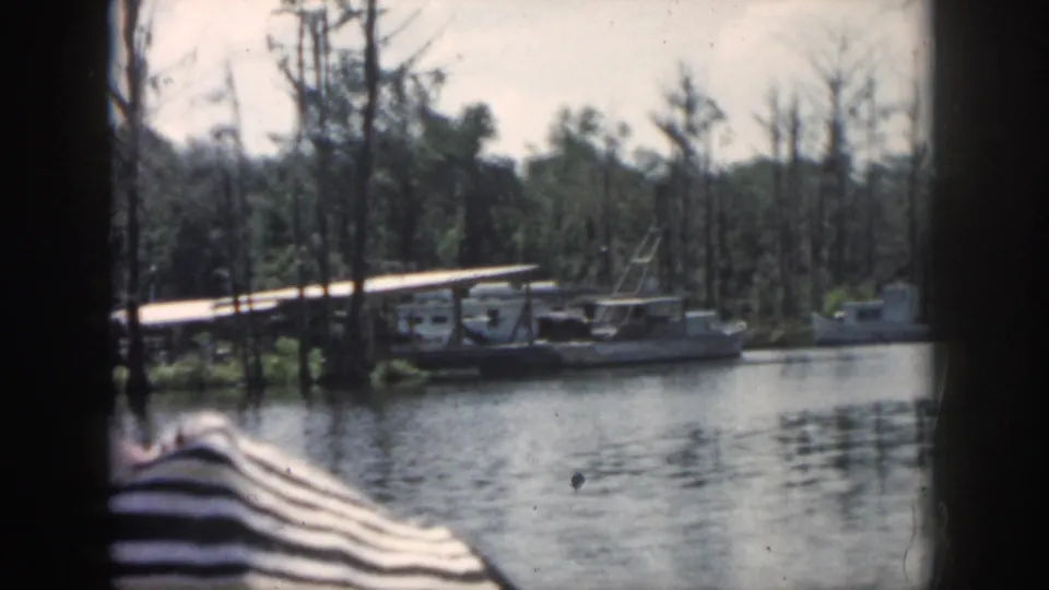 1958 New Orleans-area 8mm view of small boats tied near a low dock along a swampy shoreline.