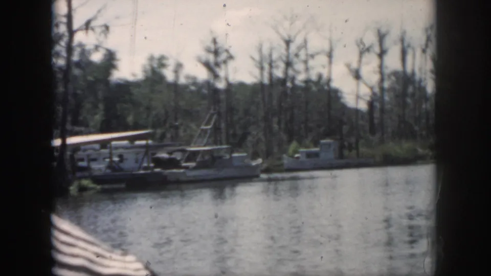 1958 New Orleans-area home-movie frame showing moored boats and a dock along a wooded swamp bank.