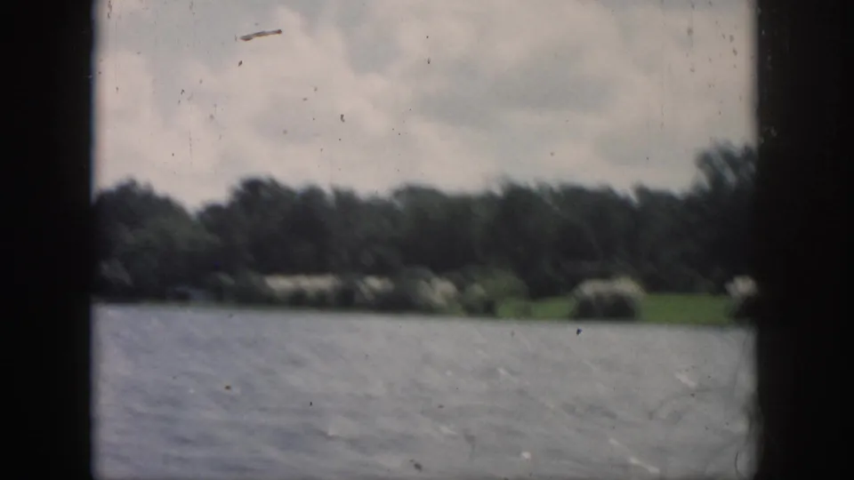 Soft 8mm frame from a 1958 boat ride near New Orleans, showing water, shoreline trees, and dark cabin or window borders.