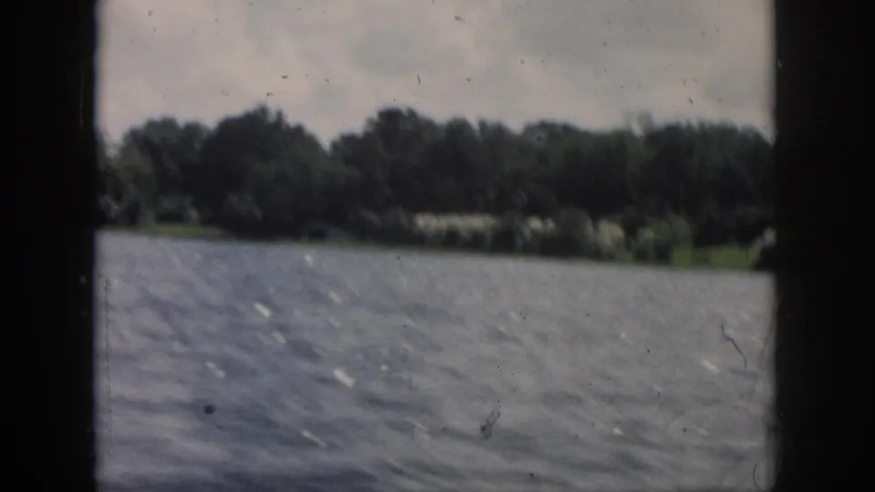 1958 8mm passenger view over choppy river water toward a blurred wooded Louisiana shoreline.