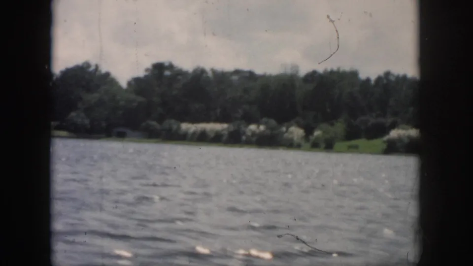 Final 1958 New Orleans-area frame with rippled river water, wooded bank, pale sky, and visible 8mm film wear.