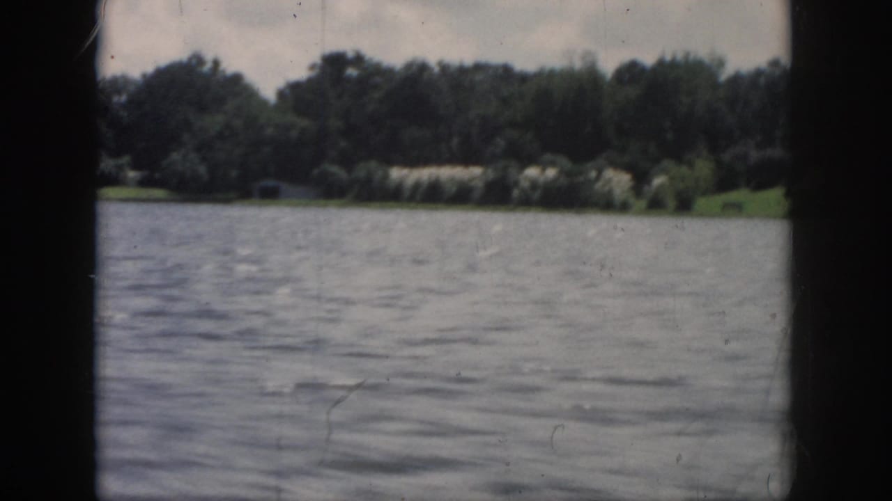 1958 New Orleans-area 8mm frame showing open water and a distant tree-lined shoreline under cloudy light.