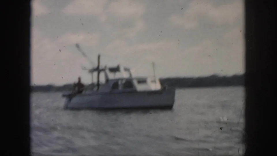 1958 home-movie frame of a small cabin motorboat on New Orleans-area water, with a person visible aboard at a distance.
