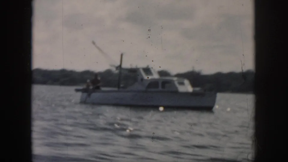 New Orleans-area 1958 8mm frame showing a small motorboat with a person aboard against rippled water and distant shore.