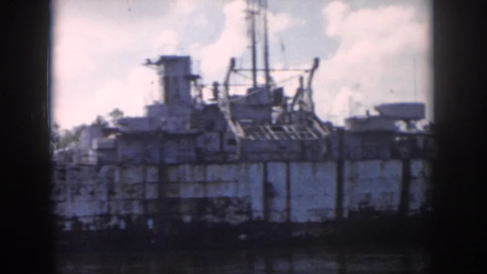 1958 New Orleans 8mm view of a docked weathered ship with deck structures and rigging beside the water.