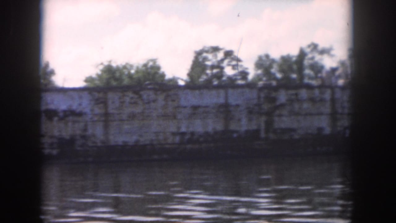 1958 New Orleans river view of a weathered white vessel and shoreline trees, framed by a boat window.