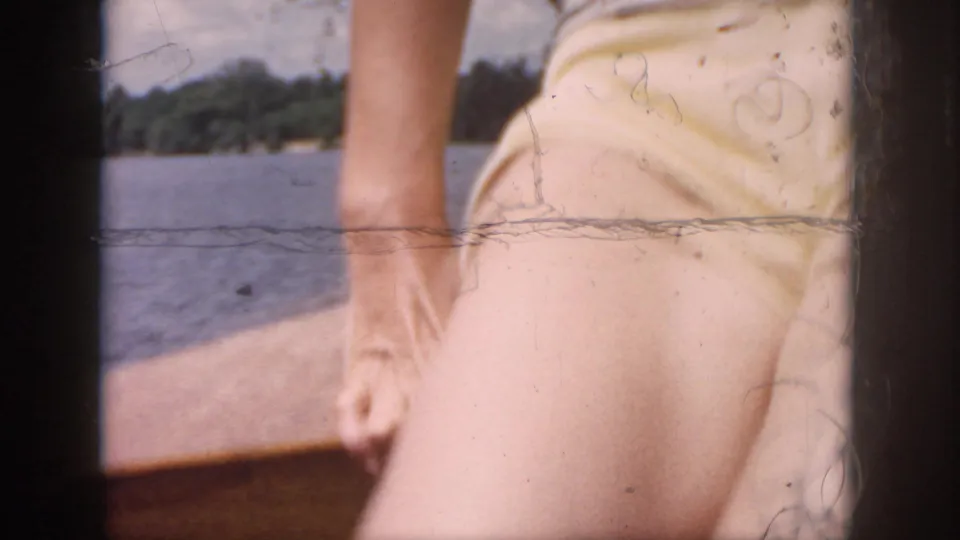 A vacationer in light summer clothing stands near a boat rail on the New Orleans river, with shoreline visible beyond.