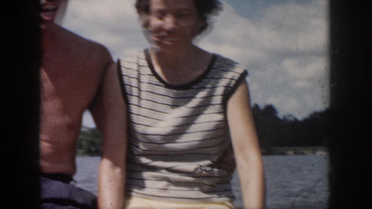 Woman in a striped sleeveless top seated beside a partly cropped shirtless man near water.
