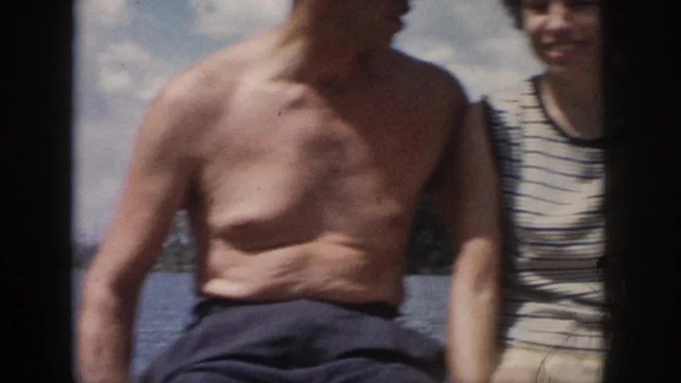 Handheld 8mm frame from the 1958 New Orleans clip, cropped tightly on the couple seated close together by the water.