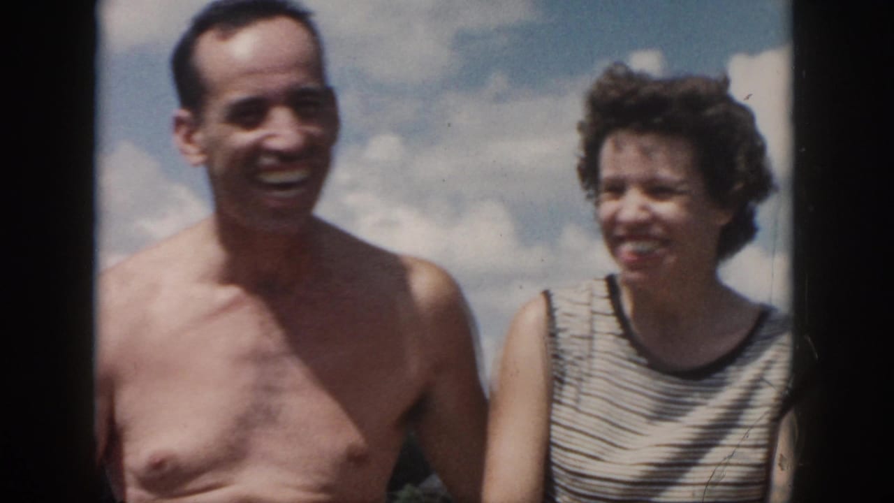 1958 New Orleans home-movie frame of a smiling adult couple, with a shirtless man and a woman in a sleeveless striped top.
