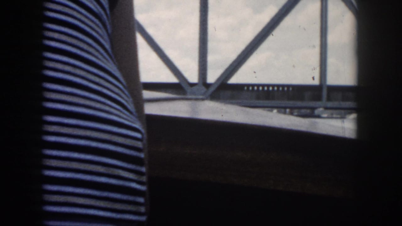 Boat-window view with a striped torso in the foreground and a metal truss bridge outside.