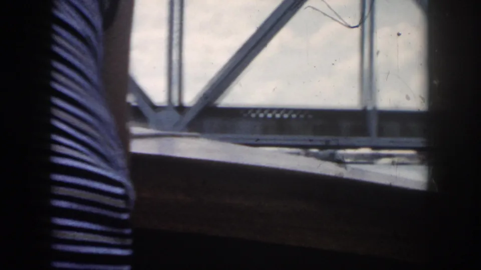 Interior boat view showing part of a person in striped clothing beside a window looking toward a metal truss bridge.