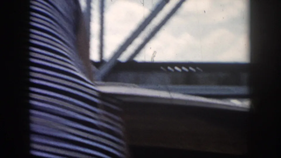 A dark-framed boat window looks out at a metal truss bridge while striped clothing fills much of the foreground.