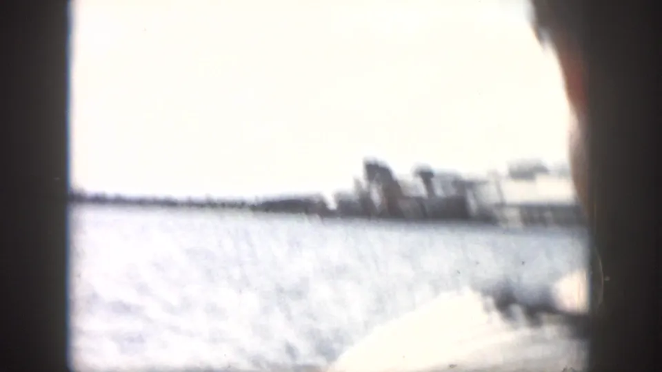 1958 New Orleans boat-tour view with bright water, distant shoreline structures, and a passenger edge in the foreground.