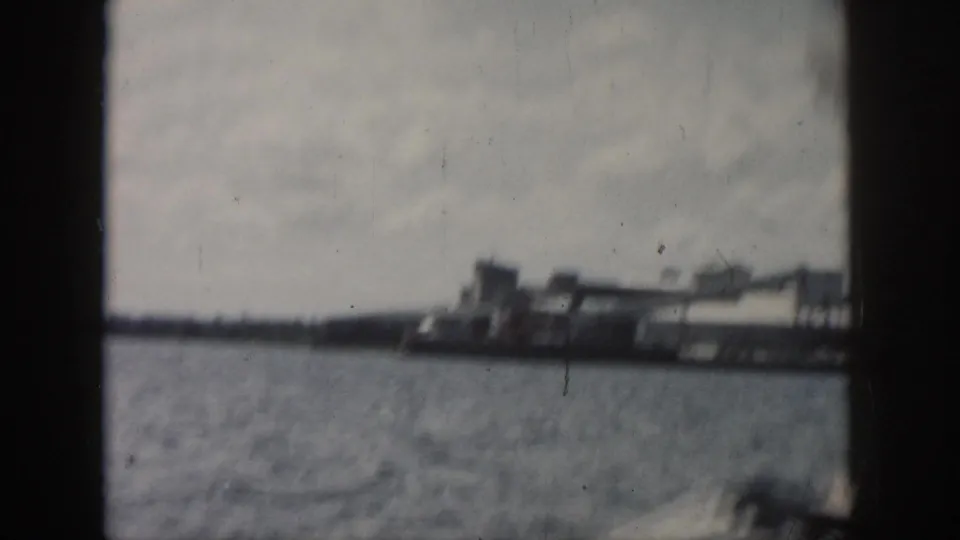 New Orleans 1958 home-movie frame showing water and distant industrial-looking shoreline structures through the boat window.