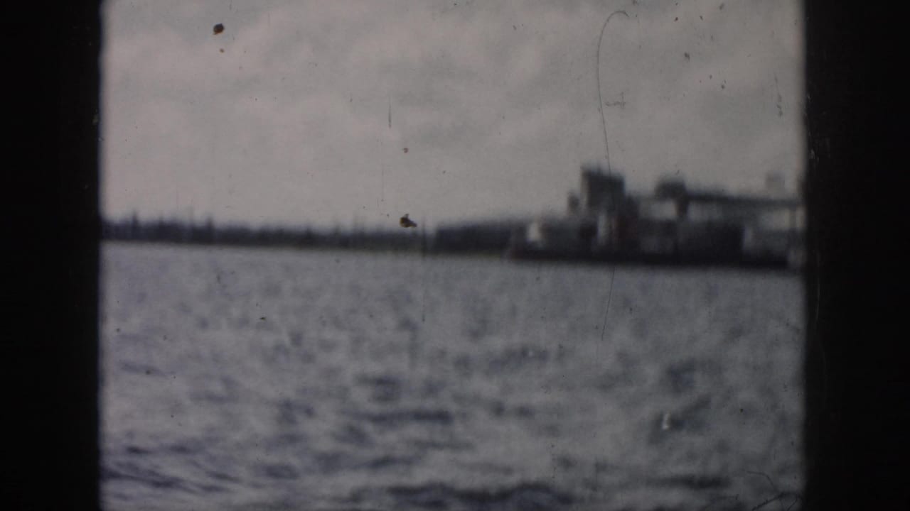 Distant New Orleans waterfront structures appear across open water, framed by dark edges of the boat or camera gate.