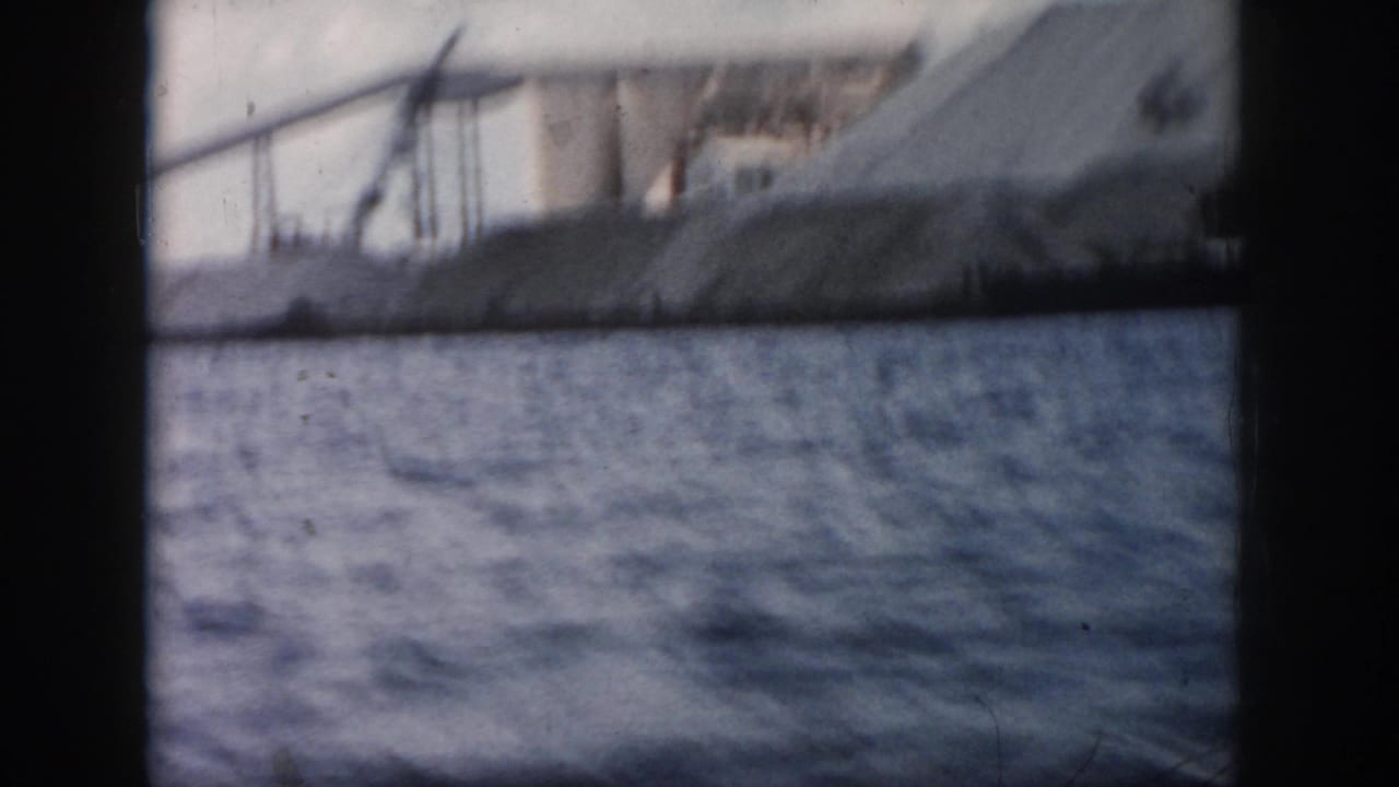 1958 New Orleans 8mm boat-view frame looking across river water toward soft, blurred industrial shoreline structures.