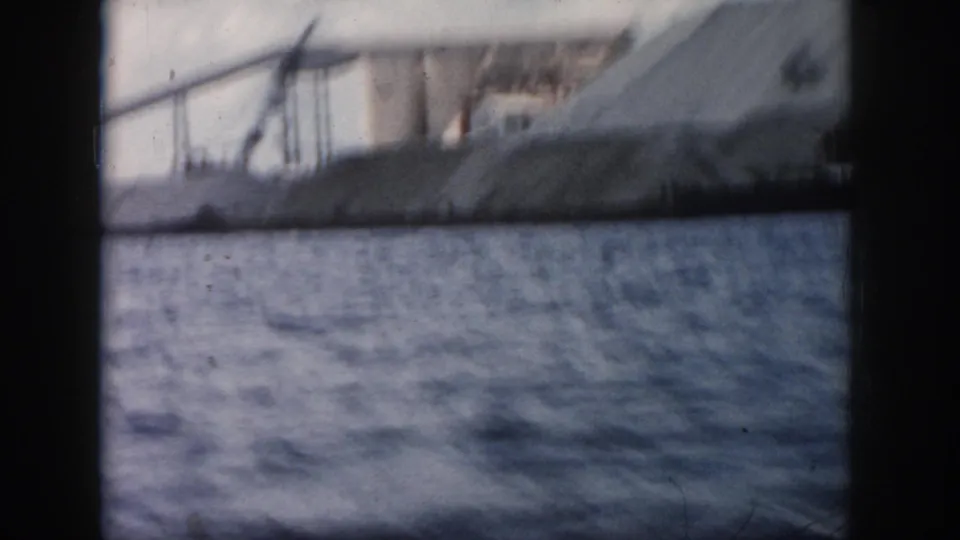 1958 New Orleans 8mm boat-view frame looking across river water toward soft, blurred industrial shoreline structures.