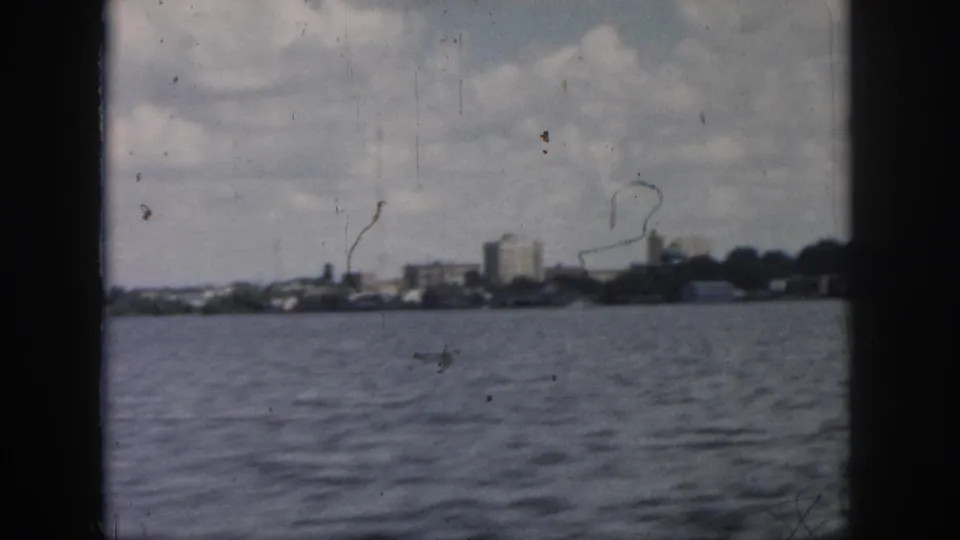 Wide 1958 New Orleans river view toward a distant city skyline and low shoreline beneath a cloudy sky.