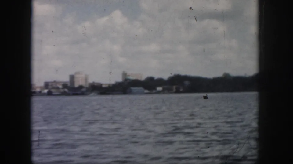 New Orleans shoreline remains in view at the end of the clip, with water foreground, low buildings, trees, and aged 8mm texture.
