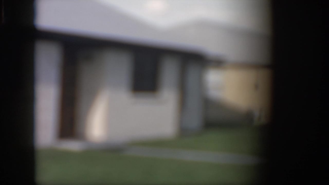 1958 New Orleans home-movie frame showing a soft, partially obscured view of a white brick ranch-style house and lawn.
