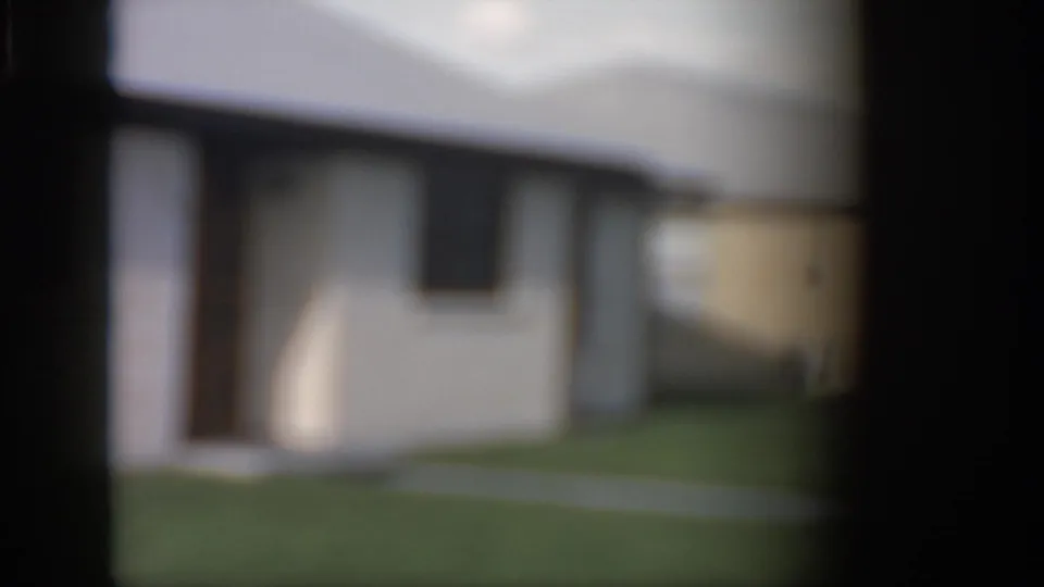 1958 New Orleans home-movie frame showing a soft, partially obscured view of a white brick ranch-style house and lawn.