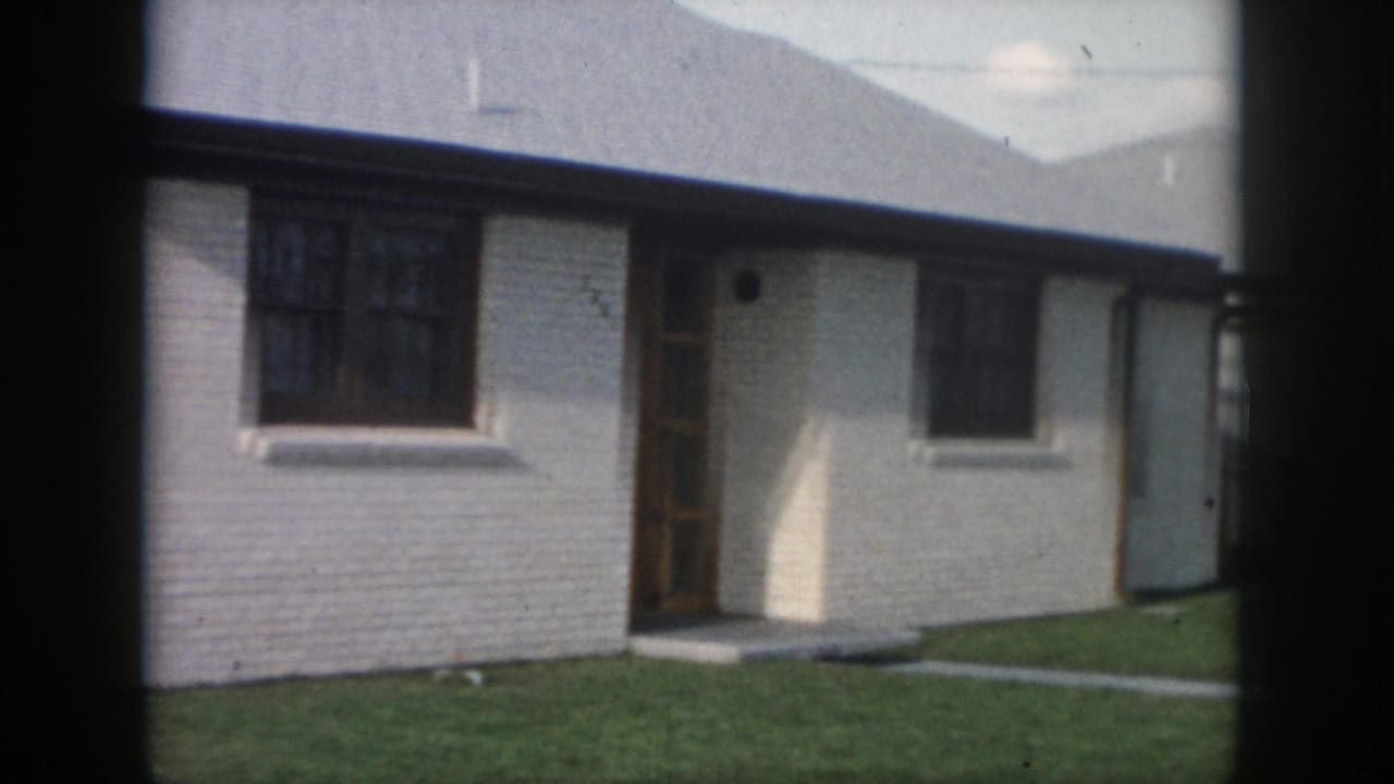 White brick house front with dark-trimmed window, wooden door, and lawn.