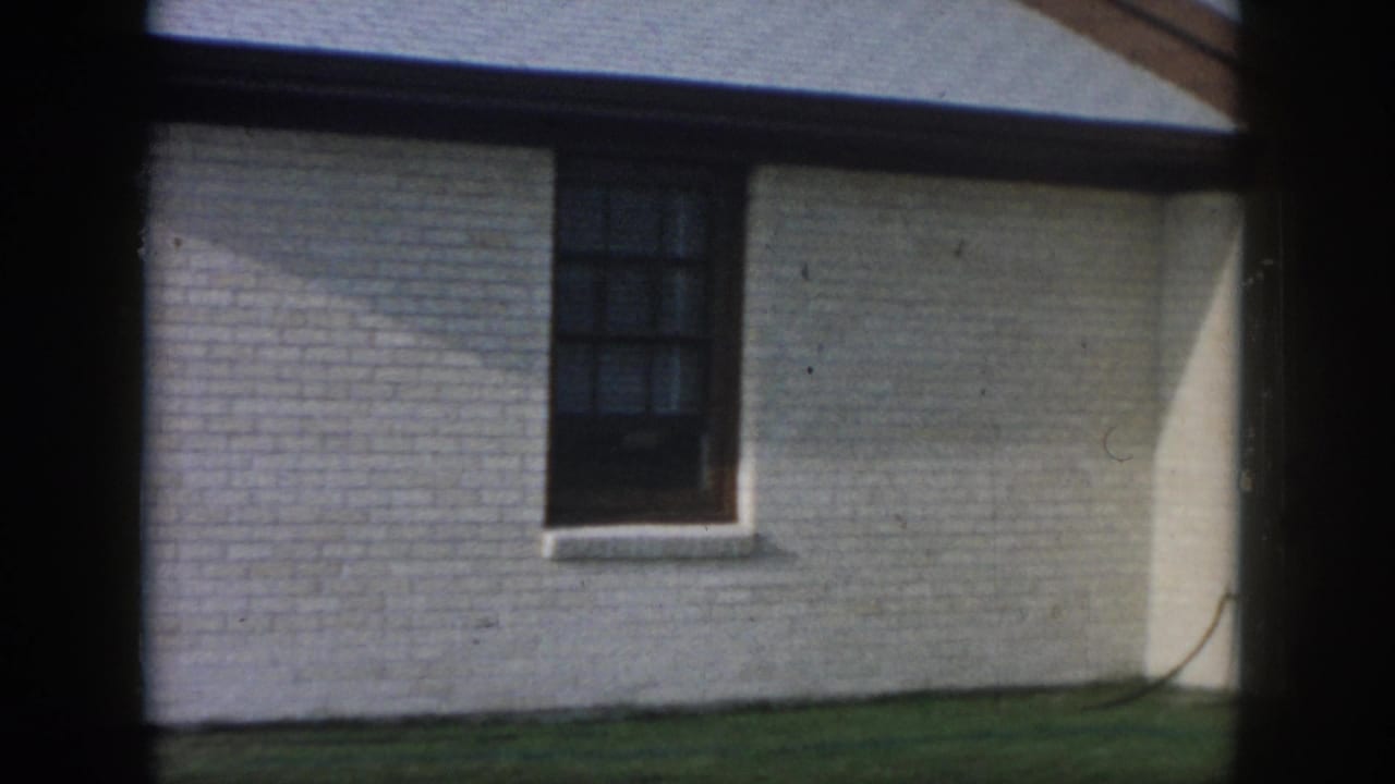 White brick exterior with a dark window, lawn, and strong shadow across the wall.