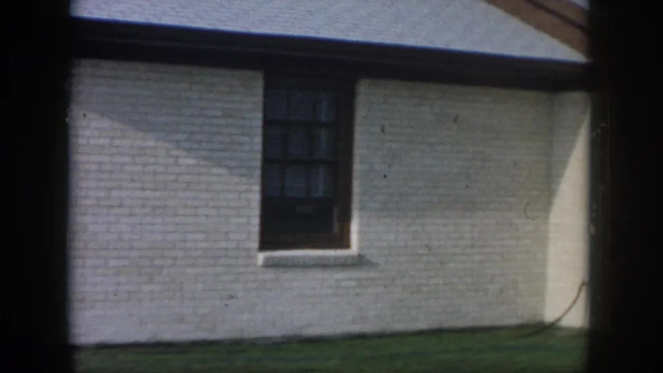 1958 New Orleans residential exterior with white brick, a dark window, lawn, roofline, and angular light shadow.