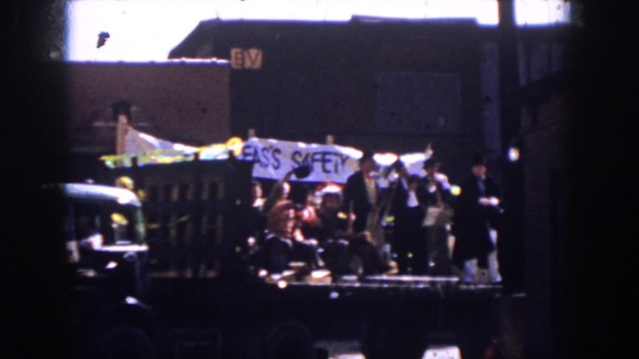 A decorated parade vehicle in Virginia carries several visible participants beneath a white banner, with buildings in the background.