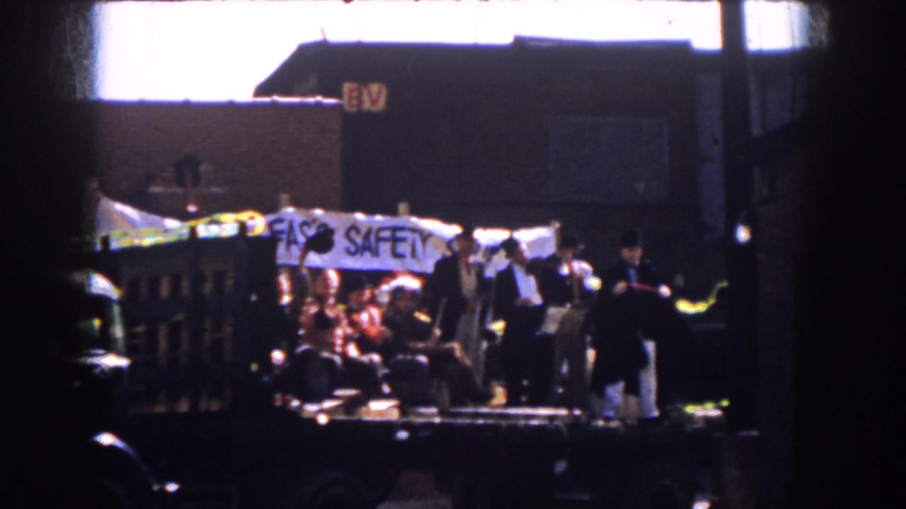 1958 Virginia home-movie frame showing parade riders on a flatbed trailer with a FAS'S SAFETY banner.
