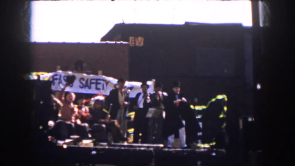 1958 Virginia parade view with suited men and seated riders on a flatbed trailer carrying a safety banner.