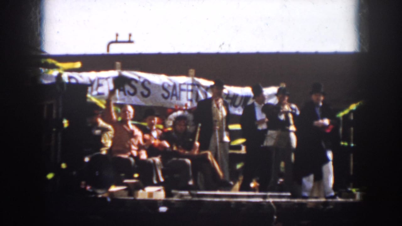 1958 Virginia home-movie frame showing men in suits and top hats on a parade float with a safety-show banner behind them.