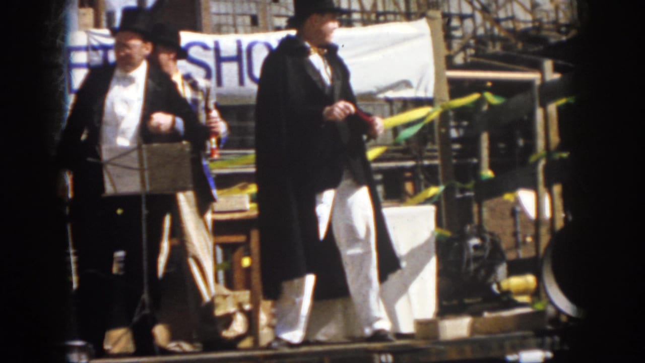 1958 Virginia 8mm frame showing formally dressed musicians on a parade float beneath a partially visible safety-show banner.