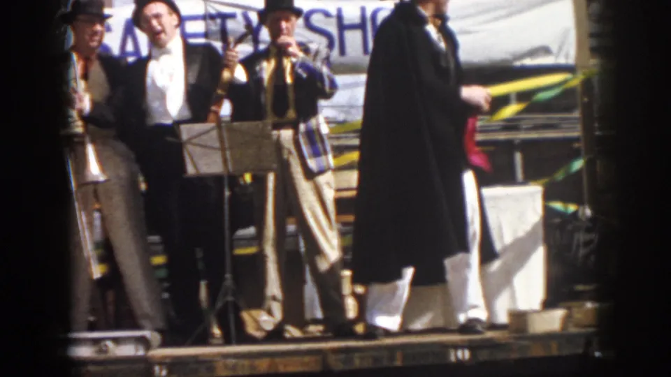 1958 Virginia parade footage frame with standing performers, trombones, music stands, and a banner partly obscured behind them.